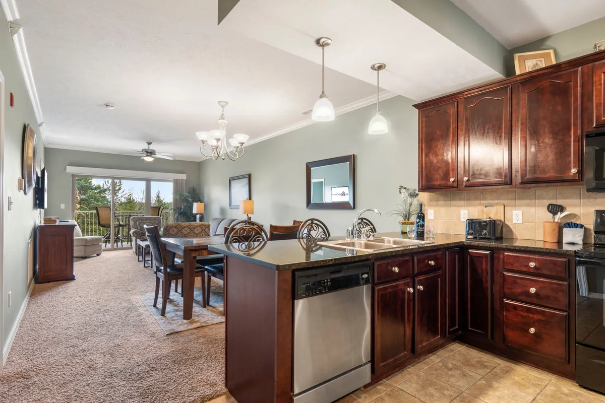 A wide-angle view featuring the open-concept living area, kitchen island, dining table, and comfortable seating. Large windows provide abundant natural light and offer views of the balcony, visually connecting the indoors with the outside environment. The stylish decor and modern furnishings create an inviting atmosphere perfect for gatherings.