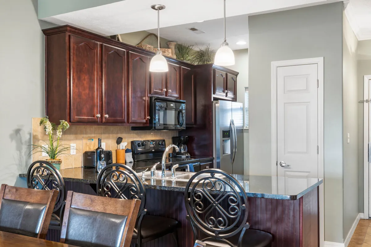 A spacious, modern kitchen featuring a central island with bar stools, gleaming stainless steel appliances, and dark wood cabinetry. The appliances are prominently displayed, including a refrigerator, oven, and microwave, with the island offering generous counter space for meal prep. The scene is set up for both cooking and casual gathering, creating a welcoming atmosphere.