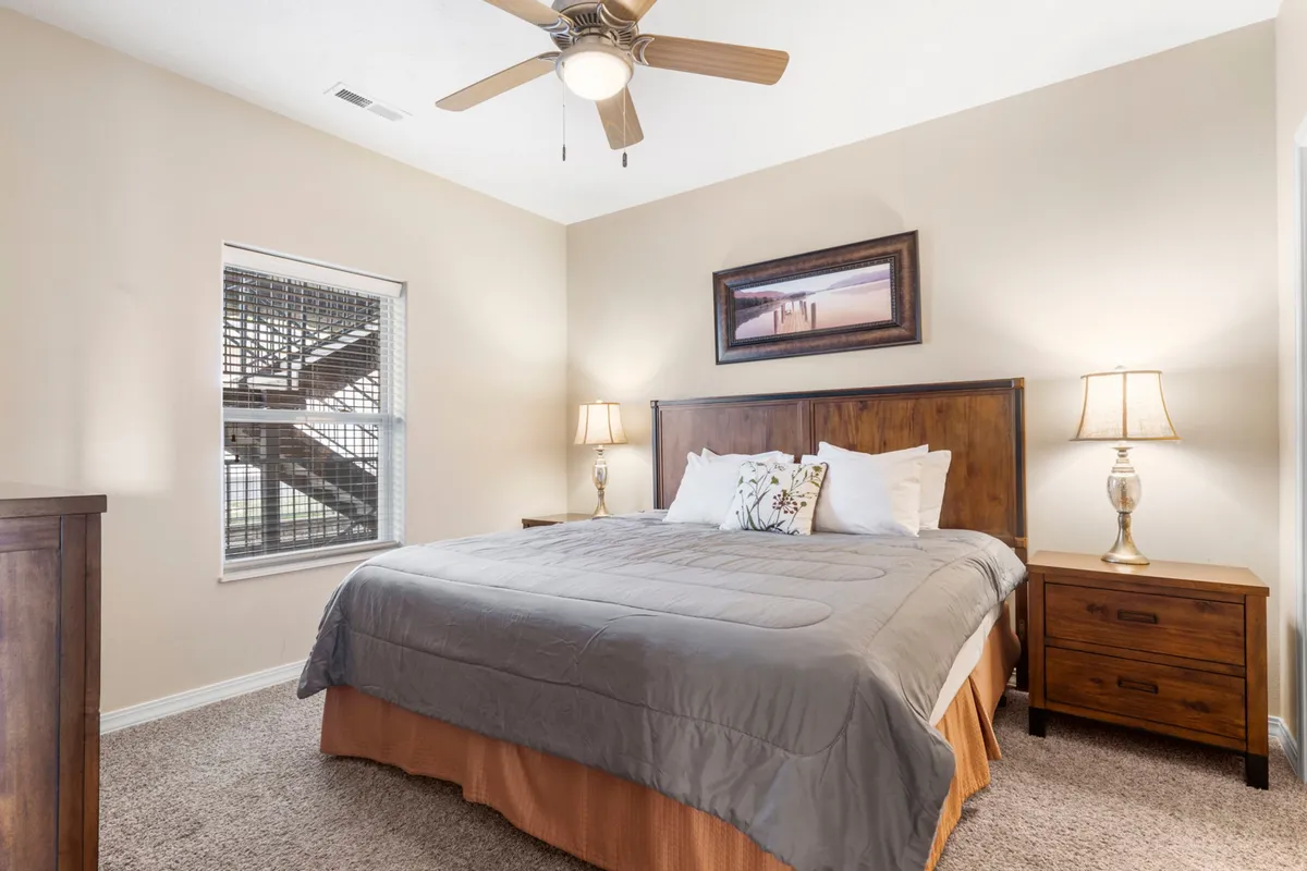 A cozy bedroom setup with a king bed, nightstands, lamps, a bright window, and calming wall art. The room is bathed in natural light, emphasizing comfort and a welcoming environment.