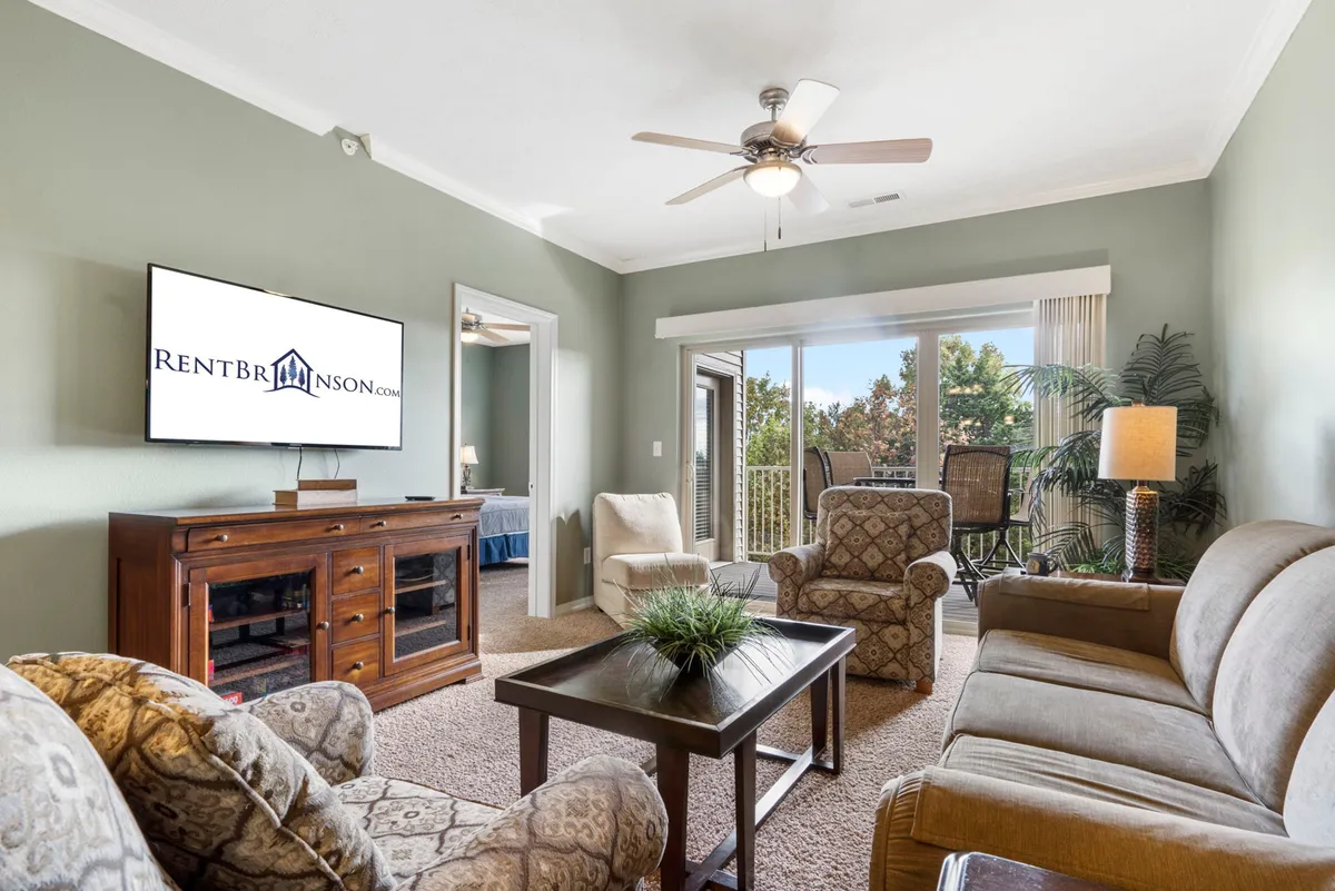 A cozy living area featuring a plush sofa, armchairs, and a coffee table, with large windows and a balcony that offers a scenic view of the outdoors. The arrangement invites relaxation while the balcony hints at the connection to natural beauty outside.
