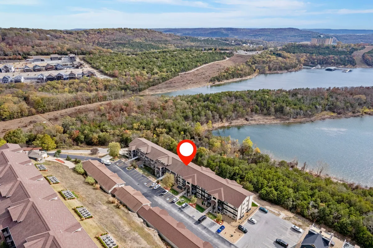 A panoramic view over Table Rock Lake at sunset, bordered by lush green forests and dotted with residential buildings. The calm water is perfect for boating, and the scene includes hints of outdoor activity areas like picnic spots.
