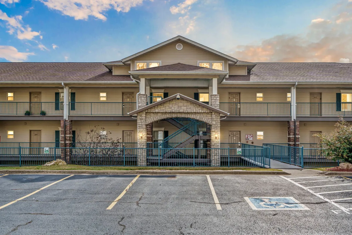 A welcoming exterior shot featuring a building with prominent balconies, landscaped grounds, and an inviting entrance archway. People can be seen relaxing on balconies, enjoying the sunset, and engaging in quiet evening activities.