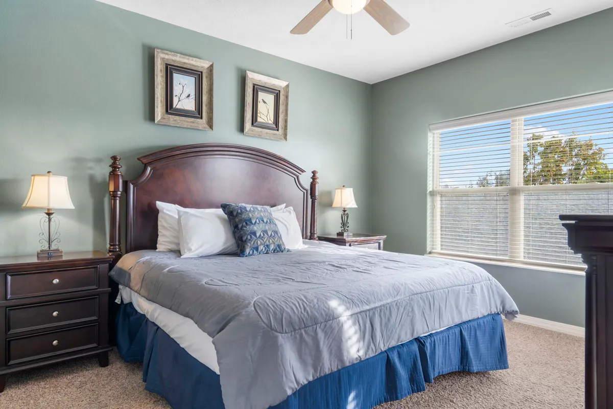 A tranquil bedroom featuring a plush king-sized bed adorned with decorative pillows, flanked by nightstands with lamps and complemented by tasteful framed artwork. Soft natural light filters in, creating a peaceful and inviting atmosphere.