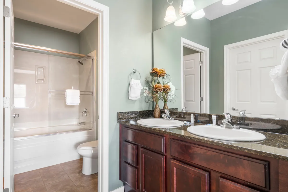 A modern, spa-inspired bathroom featuring a double sink vanity, elegant fixtures, a generous shower area, and a decorative vase with fresh flowers—exuding a sense of calm and luxury.