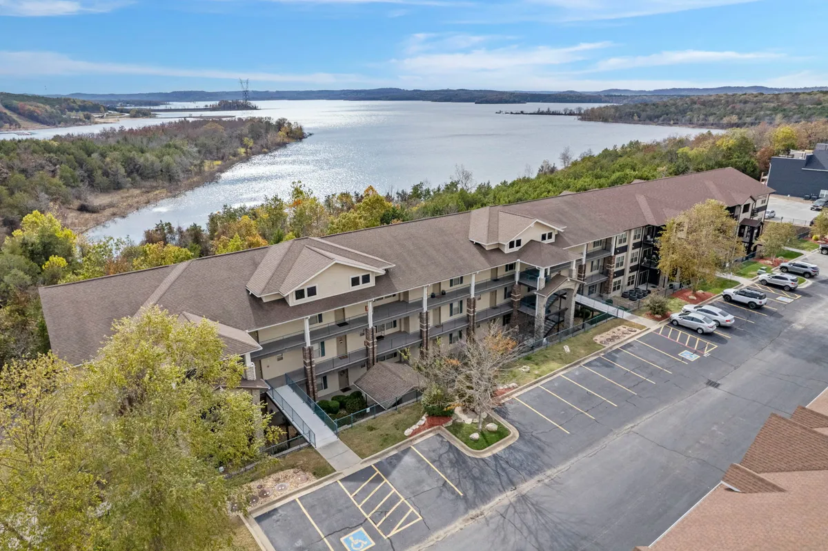 A tranquil lakeside scene at sunset, featuring still waters, natural landscape with trees, and the architectural silhouette of a condo building. The view suggests opportunities for boating, hiking, and peaceful reflection, all under a relaxing, golden sky.