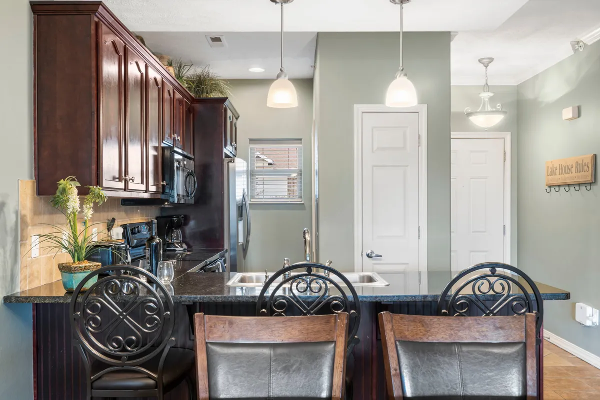 A close-up view of the kitchen's dark wood cabinetry, modern appliances, and bar seating, accented by a stylish decorative wall sign. The image creates a warm, inviting mood that emphasizes both style and functionality. The arrangement makes it easy to imagine preparing meals or entertaining guests.