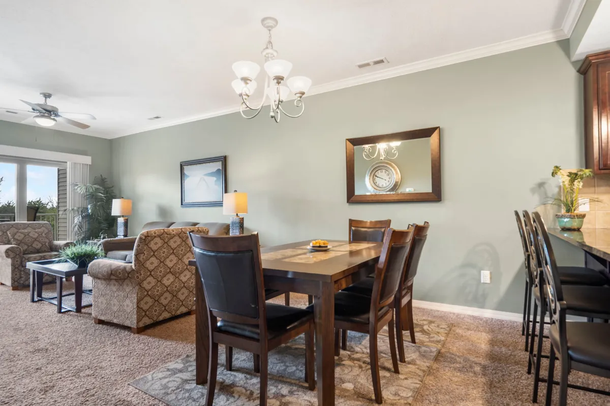 A warm and welcoming dining area featuring a stylish dining table, a sparkling chandelier, comfortable seating, and a decorative mirror. The setup is ideal for shared meals, game nights, or festive gatherings, reflecting a space designed for connection and memorable moments.