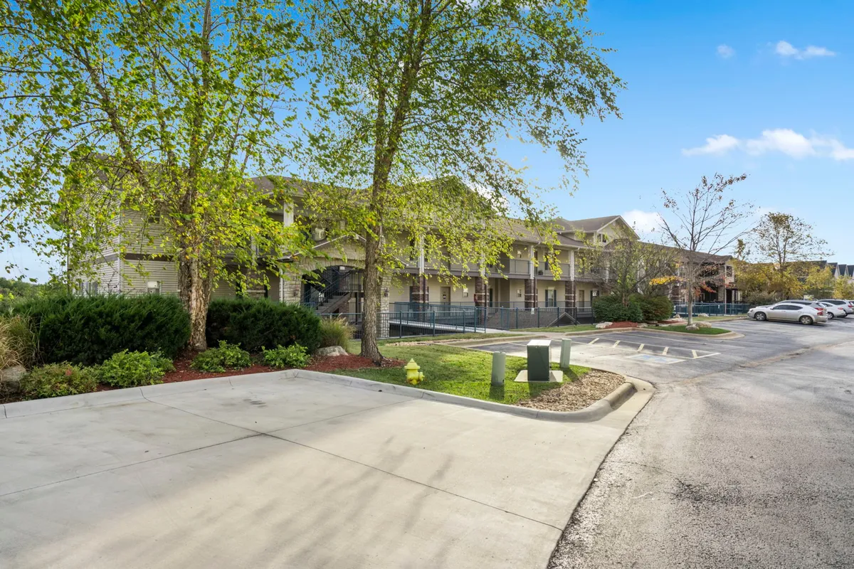 An image of the condo building's exterior, surrounded by lush green foliage and a welcoming parking area. The environment feels inviting and hints at easy access to local attractions just beyond the doorstep.