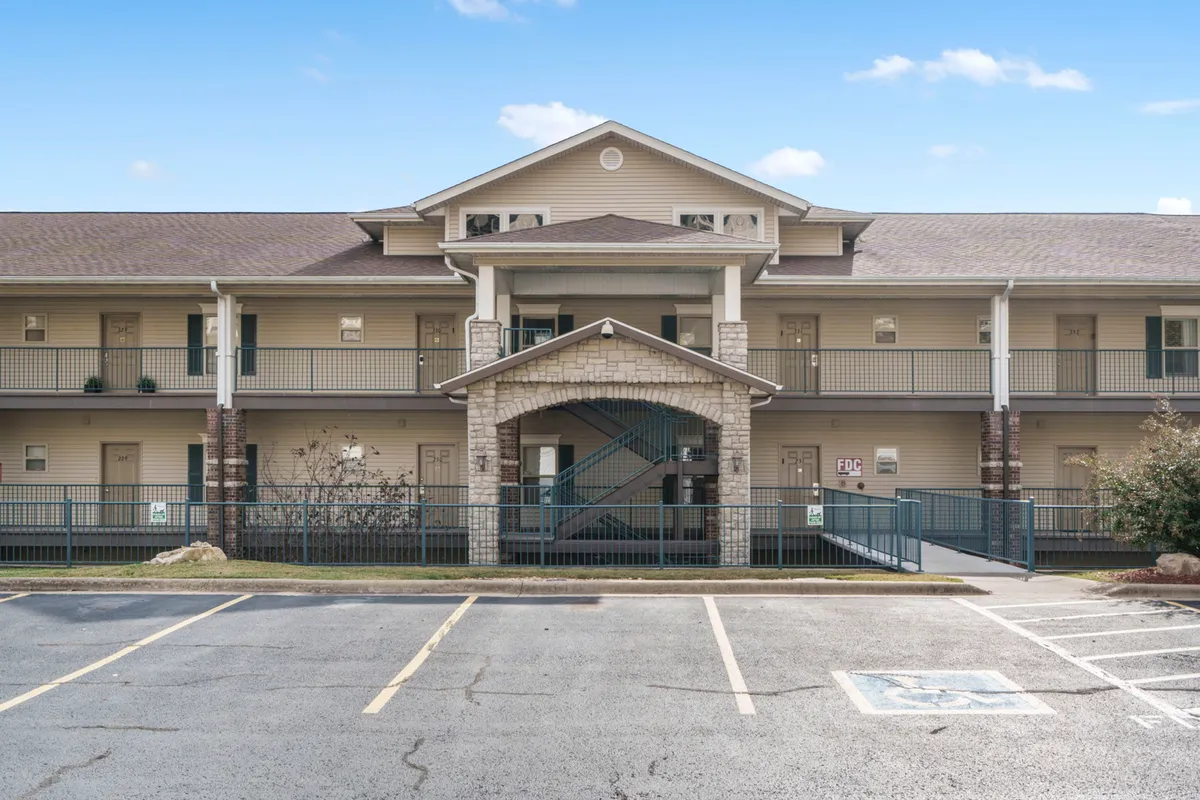 The main entrance of the property with an archway, staircases, tasteful landscaping, and a view of the parking lot. The scene conveys a sense of arrival and community, with hints of groups gathering or setting off for a night out.