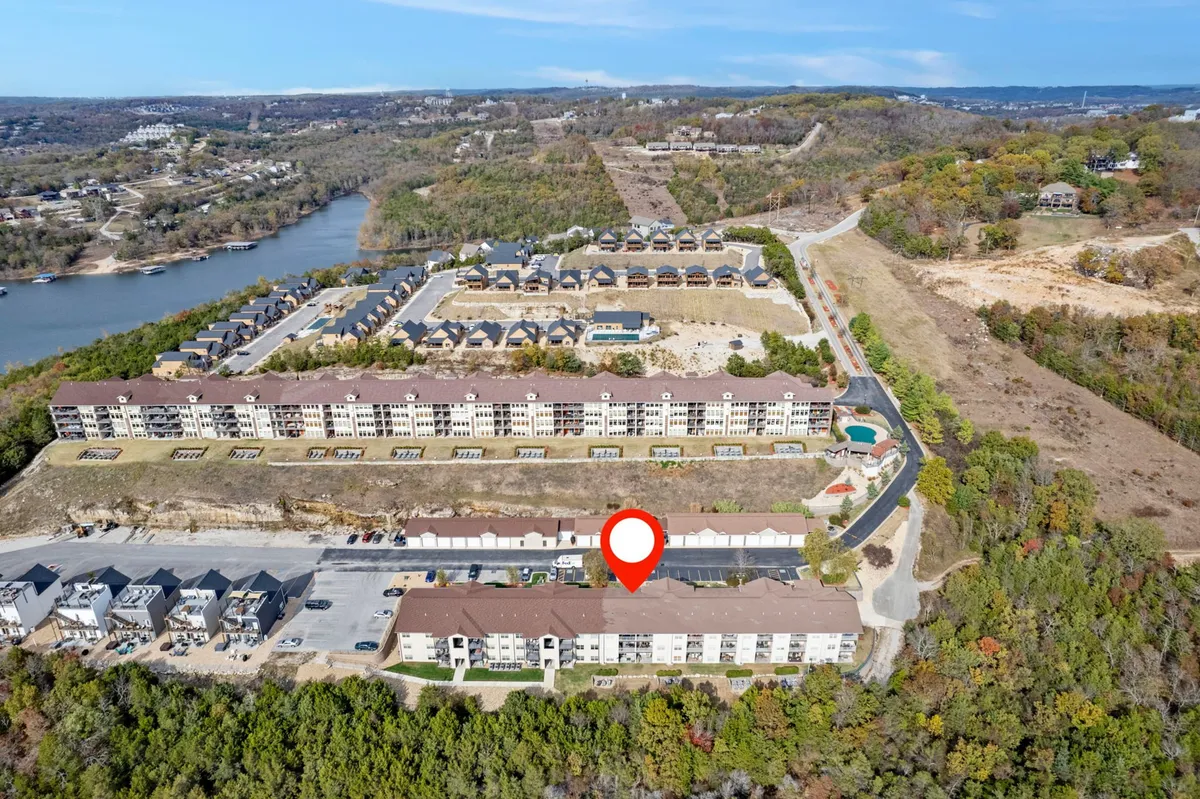 A serene exterior shot of the lakeside condo community, with apartment buildings nestled among natural greenery, overlooking Table Rock Lake. The inviting setting includes visible community amenities and areas for family gatherings and water sports.